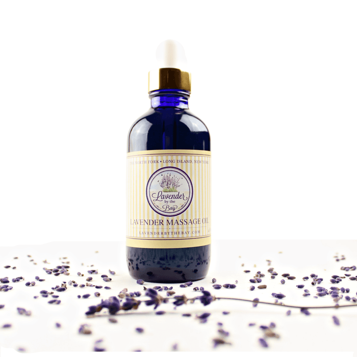 the Lavnder By The Bay Lavender Massage Oil blue bottle on white background with Lavenders flowers spread around the bottle
