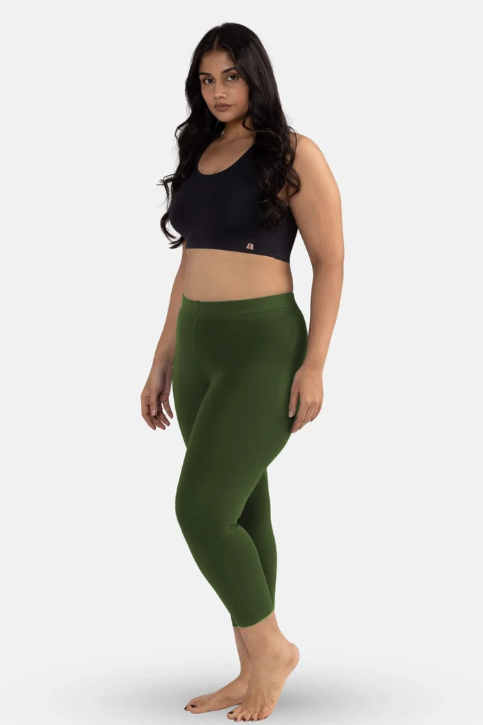 Woman wearing a black sports bra and green cropped leggings on a white background