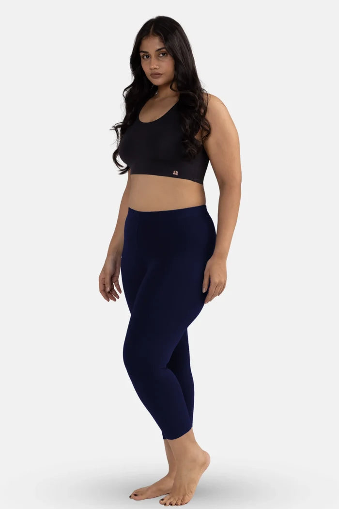 Woman wearing a black sports bra and navy blue leggings on a white background