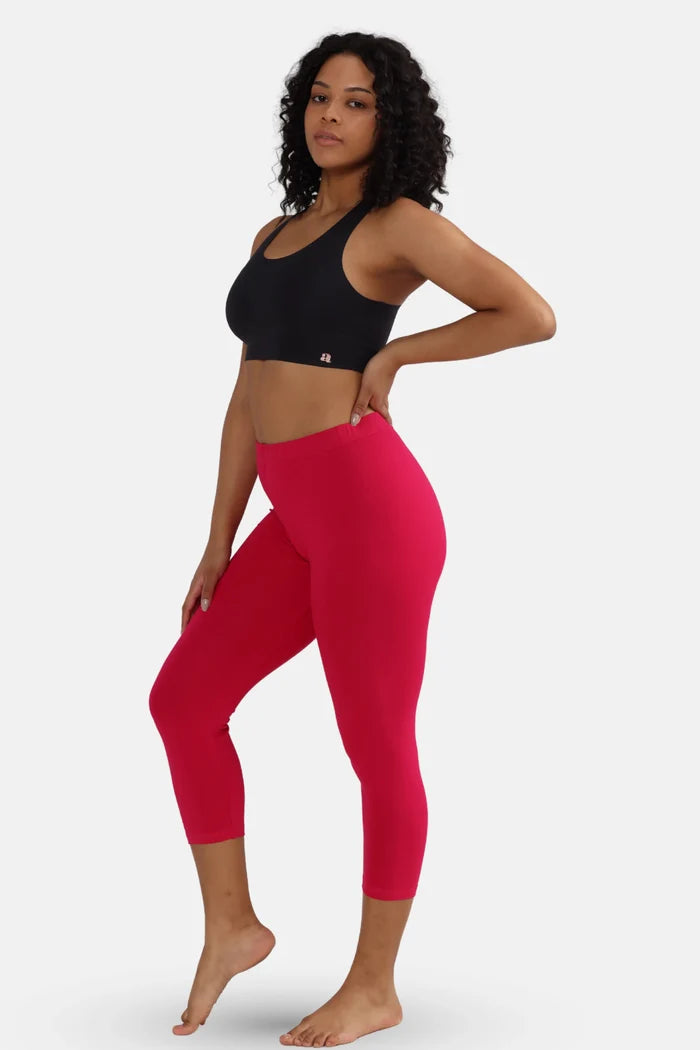 Woman wearing a black sports bra and dark pink cropped leggings on a white background