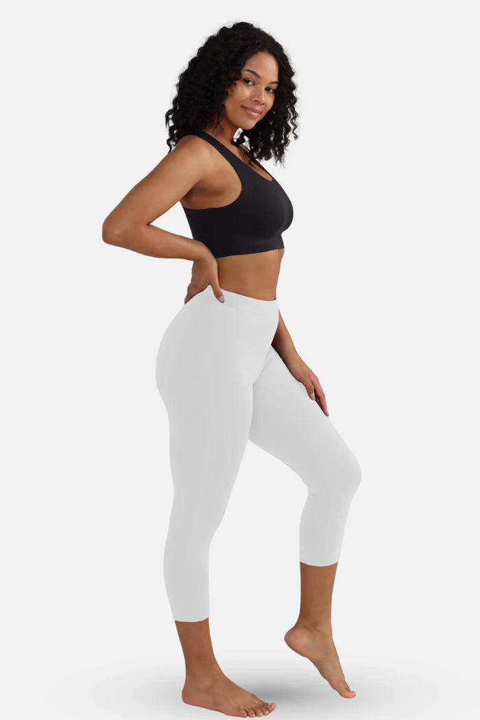 Woman wearing a black sports bra and white cropped leggings on a white background