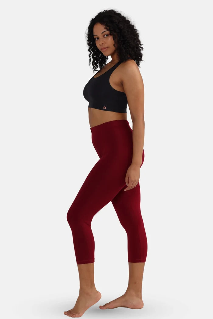 Woman wearing a black sports bra and red cropped leggings on a white background