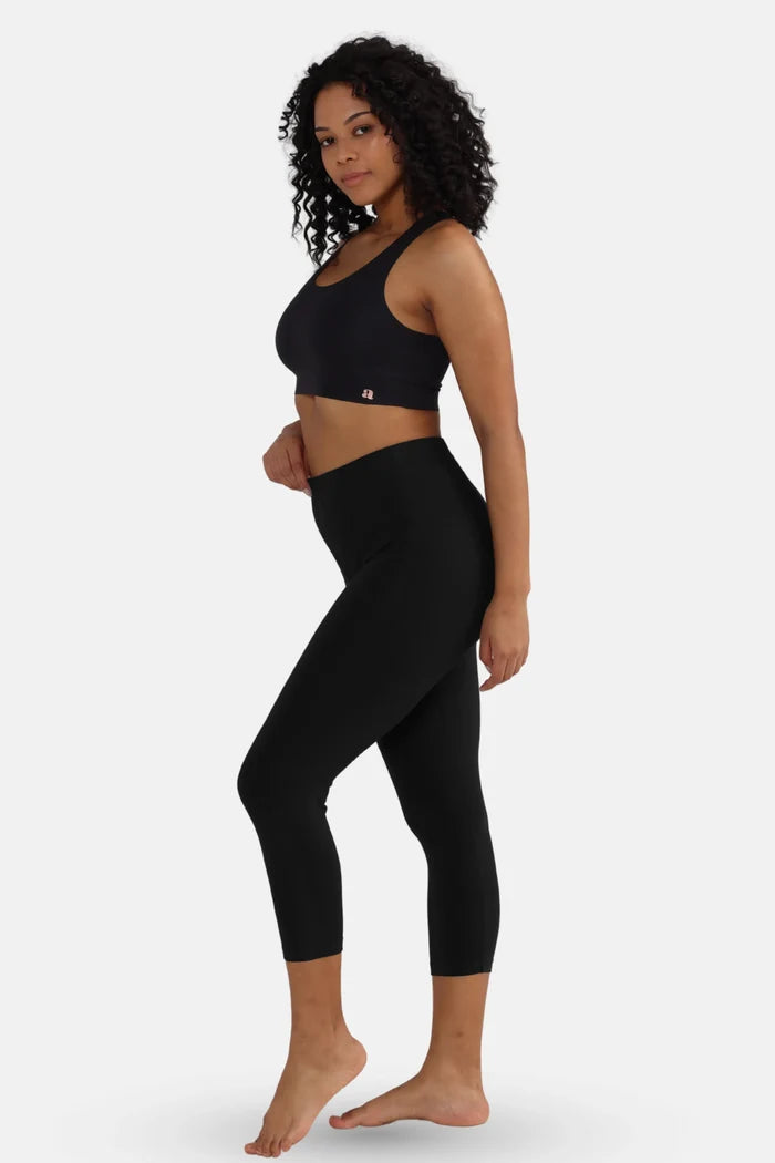 Woman wearing a black sports bra and black cropped leggings on a white background