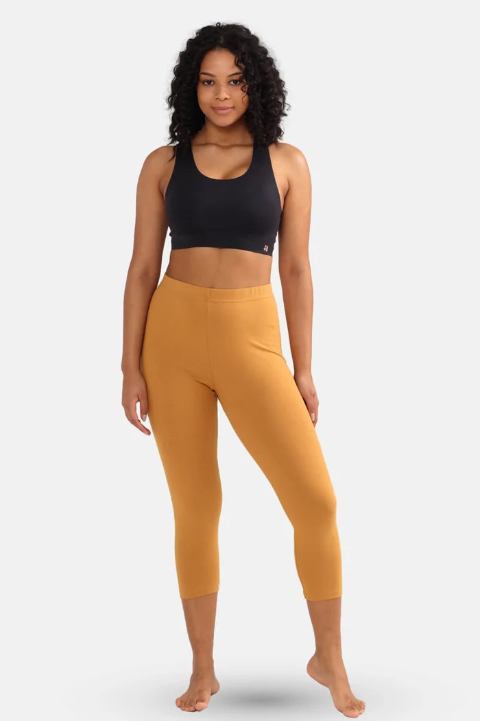 Woman wearing a black sports bra and caramel cropped leggings on a white background