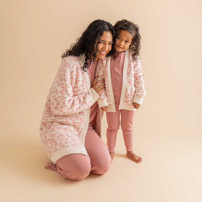 mother and young daughter wearing matching pink leopard themed print cardigans on tan background