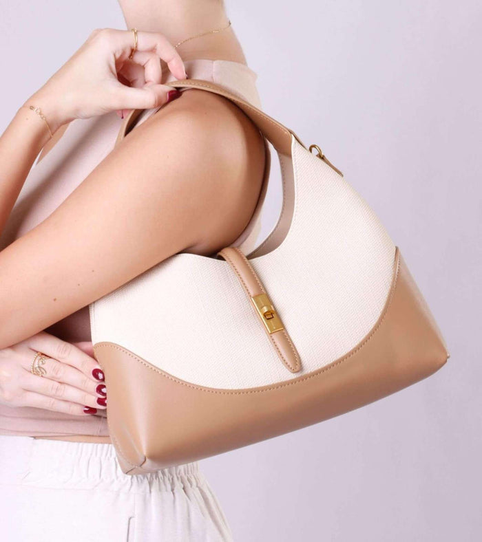 Cream and tan shoulder bag held in hand, gold clasp and front panel