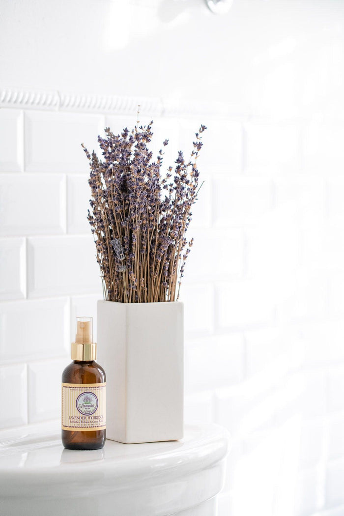 White room with white brick wall and white marble pedestal which aromatherapy spray lavender hydrosol bottle and a pot with lavenders flowers are on