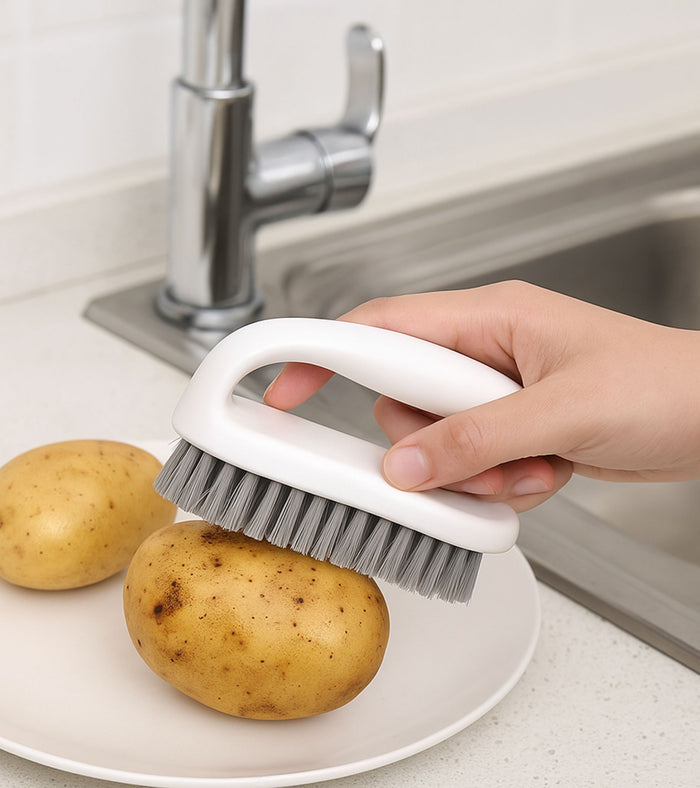 White scrub brush with gray bristles and curved handle, cleaning potatoes near sink