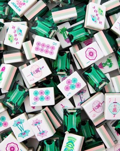 Scattered mahjong tiles with green gem frames, pink flower designs, and Joker tiles