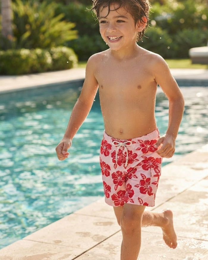 Boys swim shorts worn by child, pink base with red floral print and drawstring