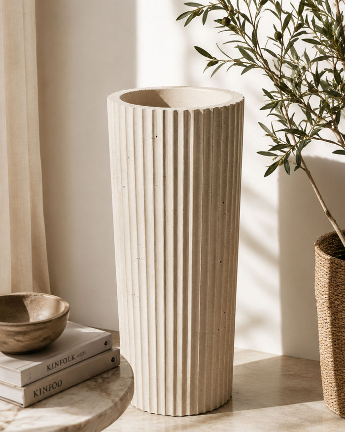 Tall fluted concrete planter with wide rim, vertical ribs, and a potted green shrub